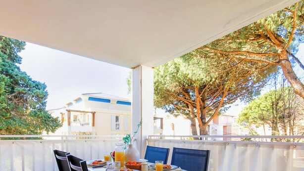 A covered outdoor dining area with a table set for breakfast, overlooking a building and trees. - Charming studio in Cavalière, pets welcome - 4 guests (Cavalière)