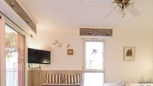 A bedroom with a bed, a television, a ceiling fan, a window with curtains, and wall decorations including seagulls and a sailboat. - Charming studio in Cavalière, pets welcome - 4 guests (Cavalière)