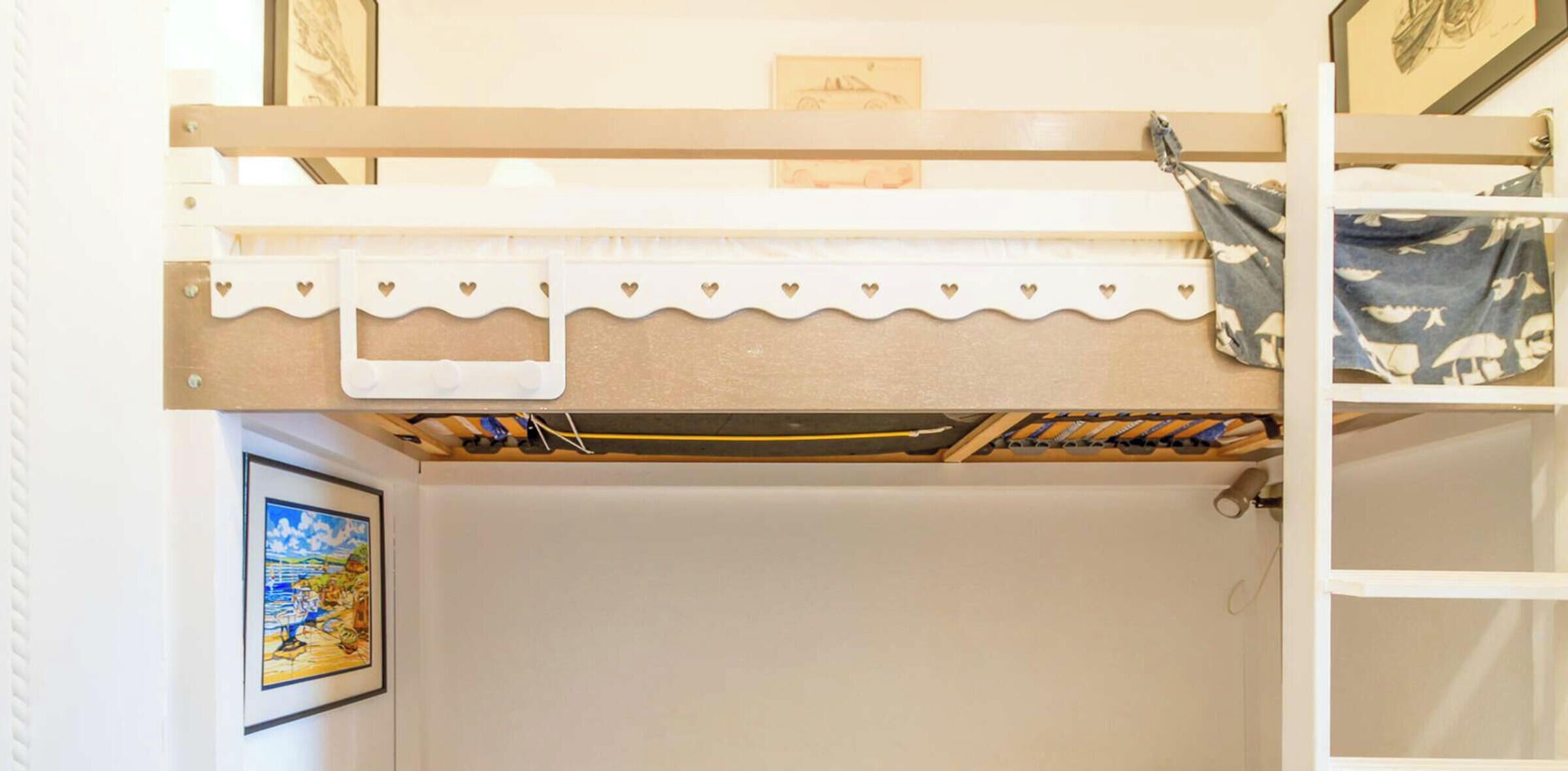 Un lit superposé avec une tête de lit blanche, une étagère sur laquelle repose un sac à motifs et un tableau encadré accroché au mur.