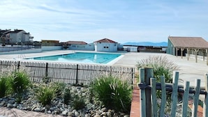 En swimmingpool med ett trädäck, ett inhägnat område med växter och byggnader i bakgrunden.