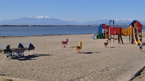 En strand med en lekplats, en bänk och ett berg i bakgrunden.