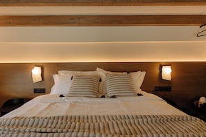 A neatly made bed with striped pillows, a textured blanket, and two wall-mounted light fixtures. - Premium Villa - Kyklio Pavilions Nafplio (Nafplio)