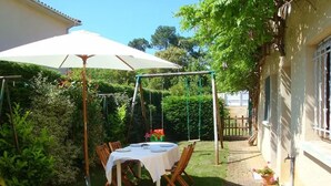 Un patio con mesa lista para comer, rodeado de follaje y un columpio.