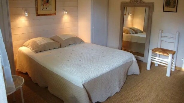 Un dormitorio con cama, una silla, armario y espejo.