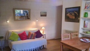 Una habitación acogedora con un sofá blanco, cojines coloridos, una mesa de comedor de madera y una lámpara.