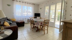 A living room with a sofa, a dining table with chairs, a TV, and a sliding glass door leading outside. - Spacious house, near the beach - 6 guests (Saint-Pierre-d'Oléron)