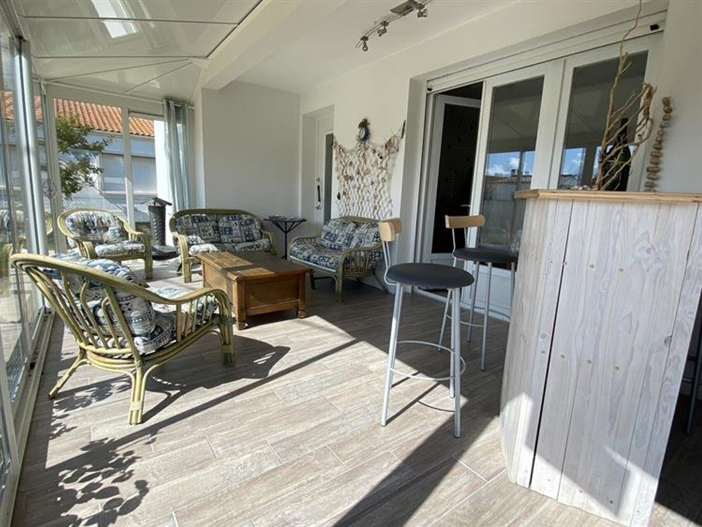 A sunlit room with wicker furniture, a wooden table, and a bar area.