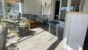 A sunlit room with wicker furniture, a wooden table, and a bar area. - Spacious house, near the beach - 6 guests (Saint-Pierre-d'Oléron)