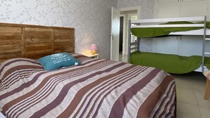 A bedroom with a striped bedspread, a wooden headboard, bunk beds, a nightstand with a lamp, and a patterned wall. - Spacious house, near the beach - 6 guests (Saint-Pierre-d'Oléron)