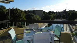 A balcony with a table and chairs, overlooking a cityscape with buildings and trees. - Apartment with parking, air conditioning - 4 guests (Bormes-les-Mimosas)