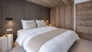 A bedroom with a brick wall, wooden ceiling, a large bed, bedside tables, and a wooden wardrobe. - Modern apartment at Mont d'Arbois - 6 guests (Megève)
