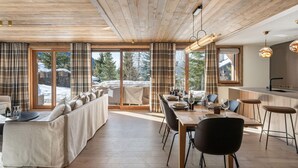 A modern interior with a wooden ceiling, a dining area with a long table and chairs, a sofa, and large windows with curtains. - Modern apartment at Mont d'Arbois - 6 guests (Megève)
