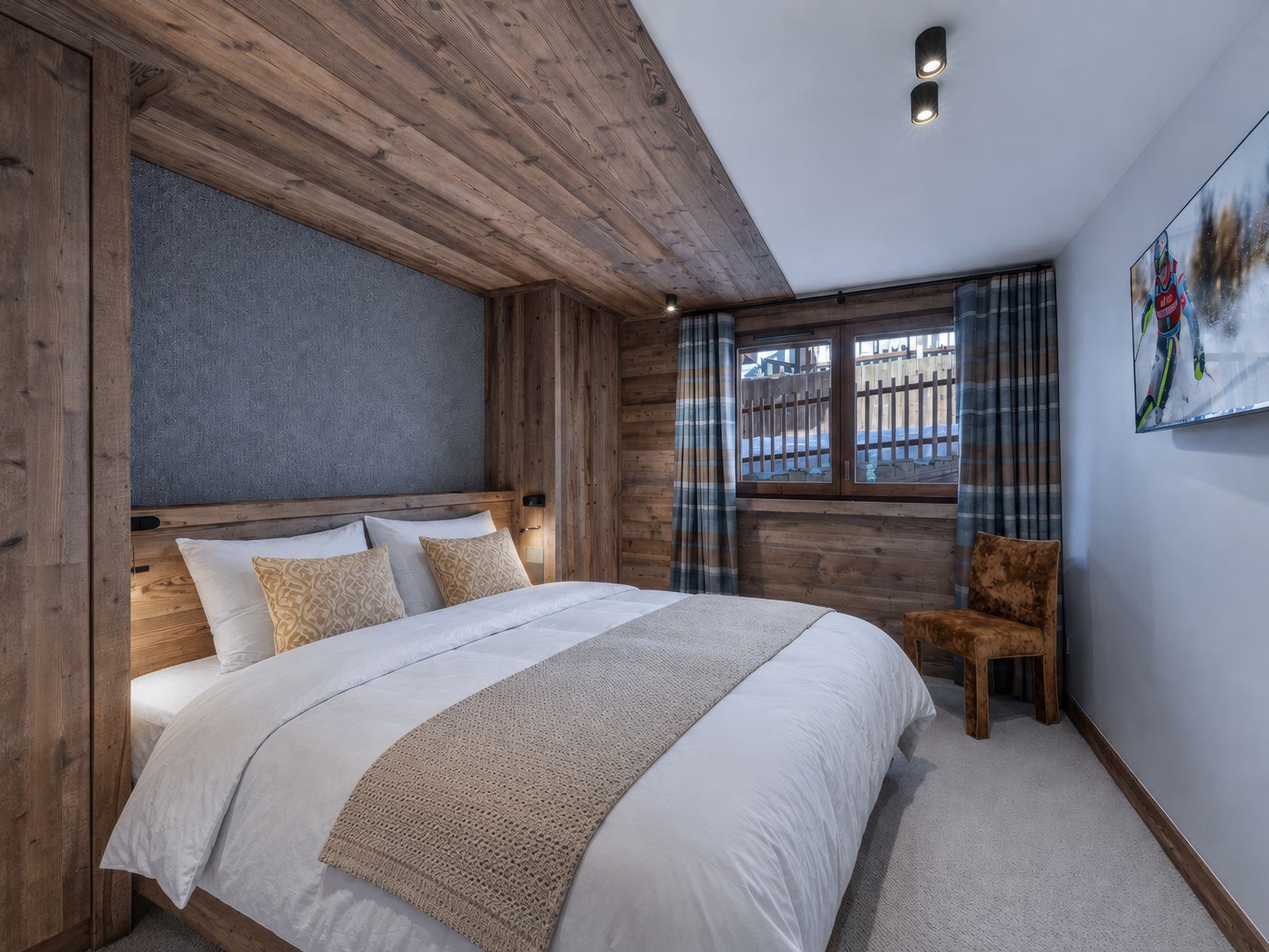 A bedroom with a wooden headboard, a large bed with white bedding, a window with curtains, and a chair.