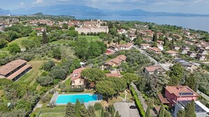 An aerial view of a residential area with a large castle, a swimming pool, and a body of water in the background. - Olive Garden Garda - pool & view Gardagate (Moniga del Garda)