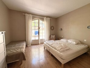 Ein Schlafzimmer mit zwei Betten, Holzboden, einem Fenster mit Vorhängen, einem Stuhl und einer Wandleuchte.