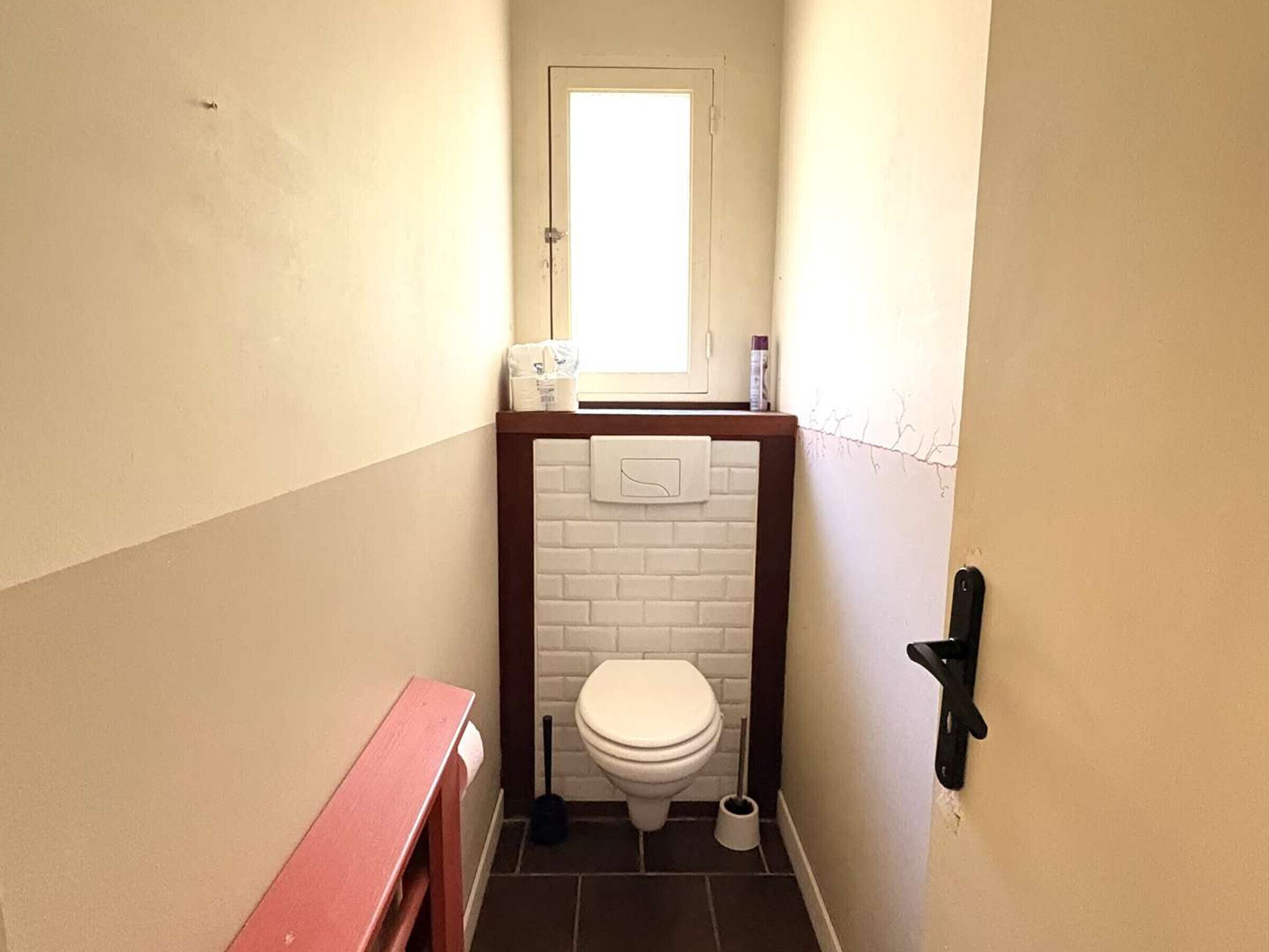 A small bathroom with a toilet, a window, a towel rack, and a toilet paper holder.