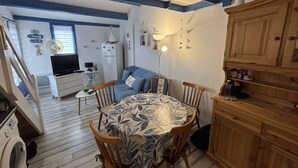 Ein gemütliches Zimmer mit Esstisch, Stühlen, einer Couch, einem Fernseher, einem Kühlschrank und einer Waschmaschine.
