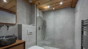 Ein modernes Badezimmer mit einem Granitwaschbecken, einer weißen Toilette, einer Duschkabine aus Glas und einer Holzbalkendecke.