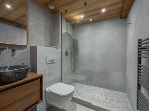 Ein modernes Badezimmer mit einem Granitwaschbecken, einer weißen Toilette, einer Duschkabine aus Glas und einer Holzbalkendecke.