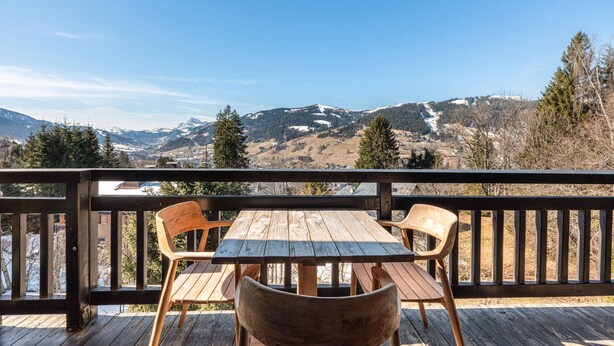 Eine Holzterrasse mit Tisch und Stühlen mit Blick auf eine gebirgige Landschaft.