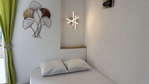 Ein schlicht eingerichtetes Schlafzimmer mit einem Bett, einer Wandleuchte und einem kleinen Regal.