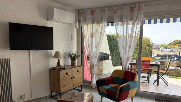 Ein Wohnzimmer mit Flachbildfernseher, Holzmöbeln, einem farbenfrohen Sessel und Blick ins Freie.