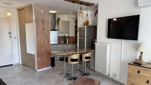 Eine moderne Küche mit Essbereich, einem an der Wand montierten Fernseher und einem Holzschrank mit Schubladen.