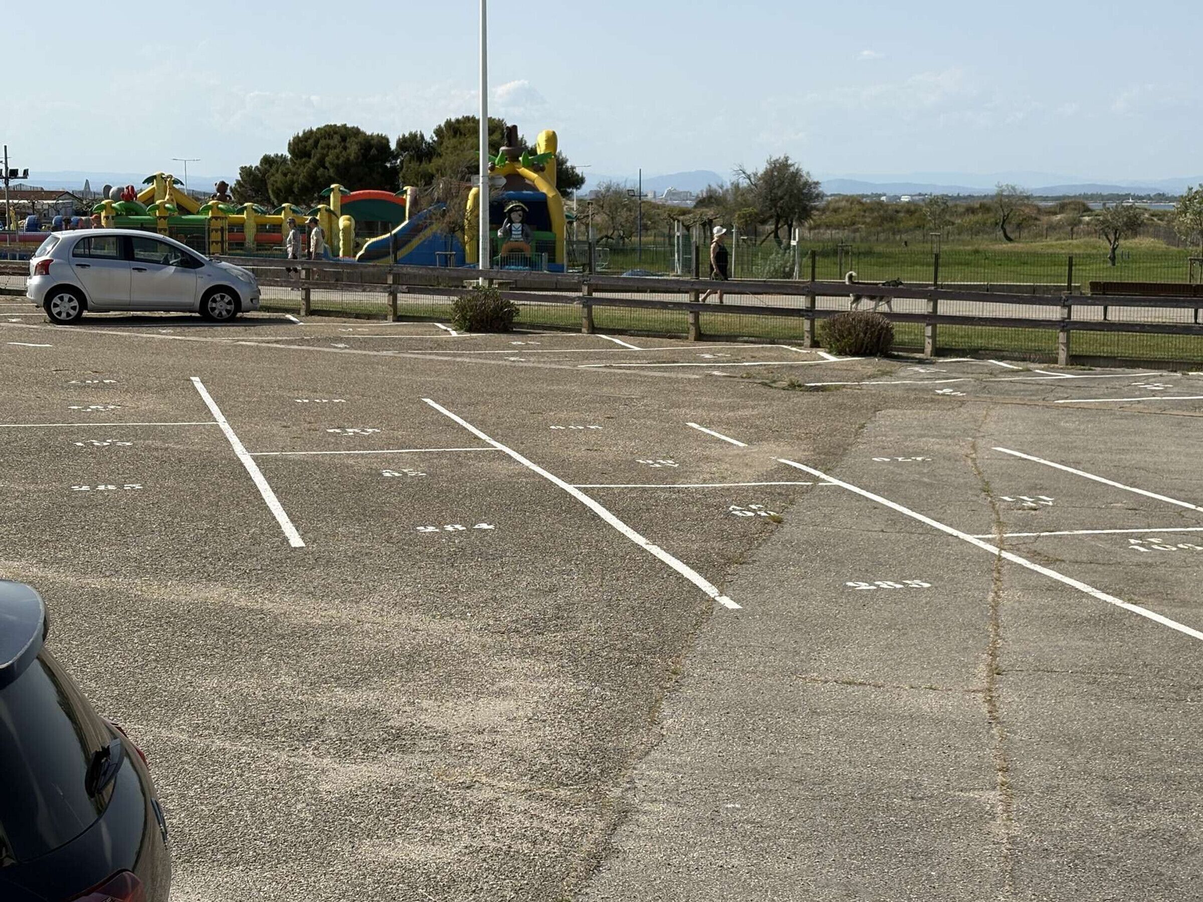 Een parkeerplaats met aangegeven parkeerplaatsen en een speeltuin op de achtergrond.