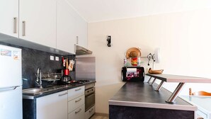 A modern kitchen with a black countertop, stainless steel appliances, and a small dining area with a bench. - Ground floor apartment near beach - 4 guests (Fleury-Saint-Pierre-la-Mer)
