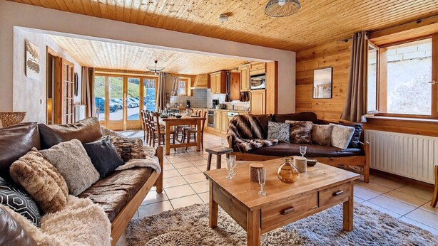 A cozy cabin interior with a wooden ceiling, a dining area, a sofa, and a coffee table.
