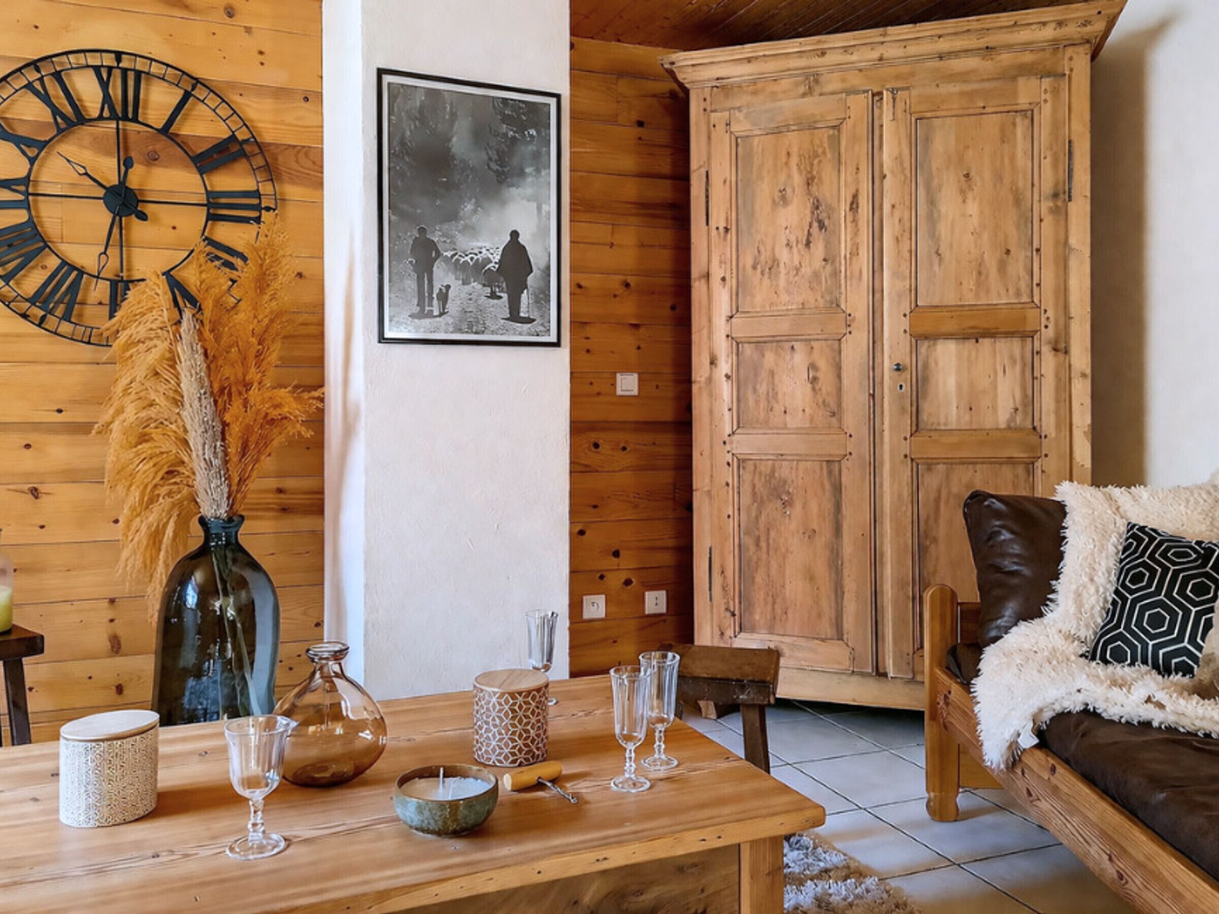 A wooden interior with a large clock, a framed photograph, and a wooden wardrobe.