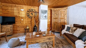 A cozy living room with wooden walls, a wooden ceiling, a large clock, a television, a sofa, and a coffee table.