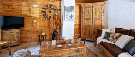 A cozy living room with wooden walls, a wooden ceiling, a large clock, a television, a sofa, and a coffee table.