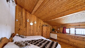A wooden cabin room with two beds, a radiator, and a window with curtains.