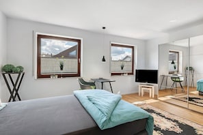 Ein modernes Schlafzimmer mit Bett, Schreibtisch, Stuhl, Fernseher und einem groĂen Spiegel.