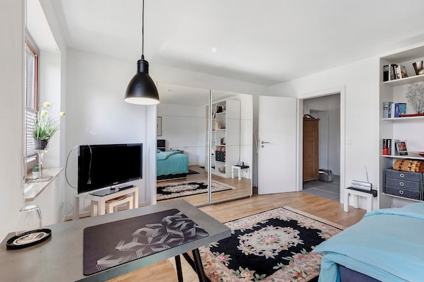 Ein modernes Wohnzimmer mit Flachbildfernseher, Esstisch, Couchtisch, Sofa, groĂem Spiegel und BĂŒcherregal.