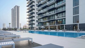 A modern building with a swimming pool, outdoor seating, and a clear view of the surrounding area. - StayShort - 1-bedroom in JVC sleeps 4 with Amazing Views and Large Balcony! (JVC)