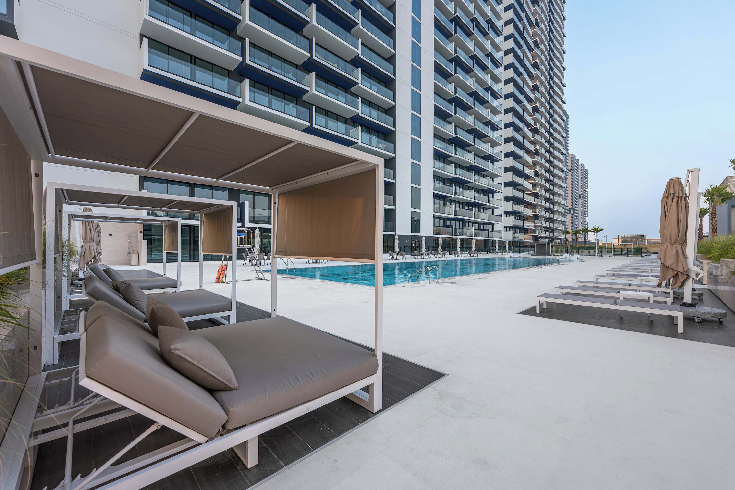 Un hotel modern amb una piscina al terrat, gandules i una zona de seients coberta.