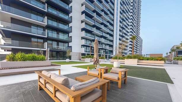 A modern outdoor seating area with wooden furniture, a covered umbrella, and a well-maintained lawn. - StayShort - 1-bedroom in JVC sleeps 4 with Amazing Views and Large Balcony! (JVC)
