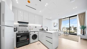 A modern kitchen with a stove, oven, and washing machine, a dining area with a table and chairs, and a large window with a city view. - StayShort - 1-bedroom in JVC sleeps 4 with Amazing Views and Large Balcony! (JVC)