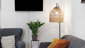 Un saló modern amb un sofà gris, una planta en test, una làmpada de peu i un televisor penjat a la paret.