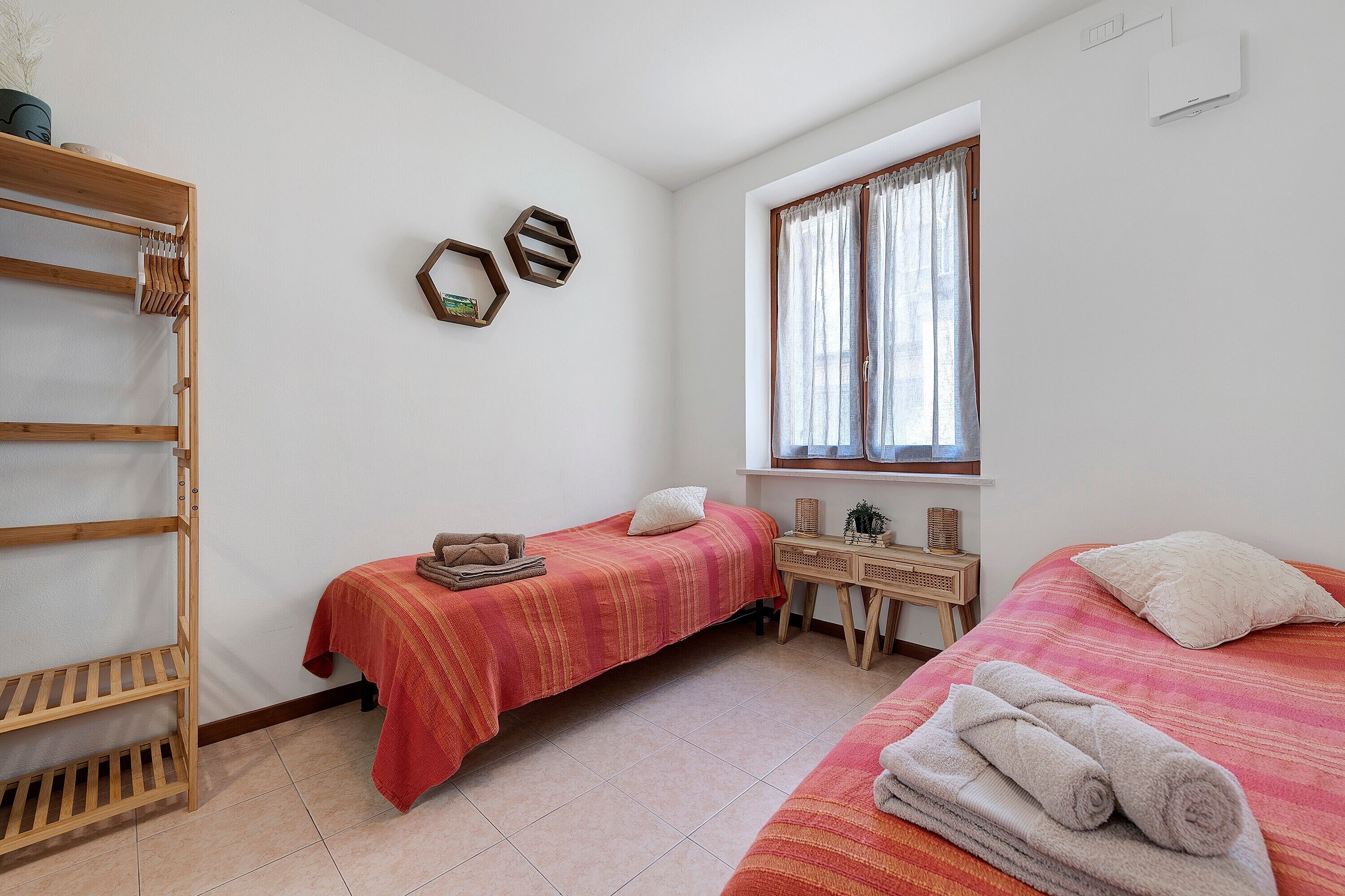 Ein Schlafzimmer mit zwei Betten, einem Holzregal, einem Schreibtisch und einem Fenster mit Vorhängen.