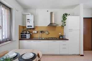 A compact kitchen with white cabinets, a microwave, a gas stove, a water heater, and a sink. - BeeHome in Verona - Cosy home near the old town - Free parking, AC in every room, Fast wifi (Verona)