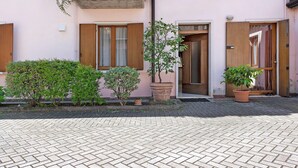 Un edifici amb un vestíbul pavimentat de maó, portes de fusta i plantes en testos.