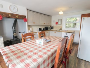 A kitchen with a table set for two, a stove, and a washing machine. - Ysgoldy (Dolwyddelan)