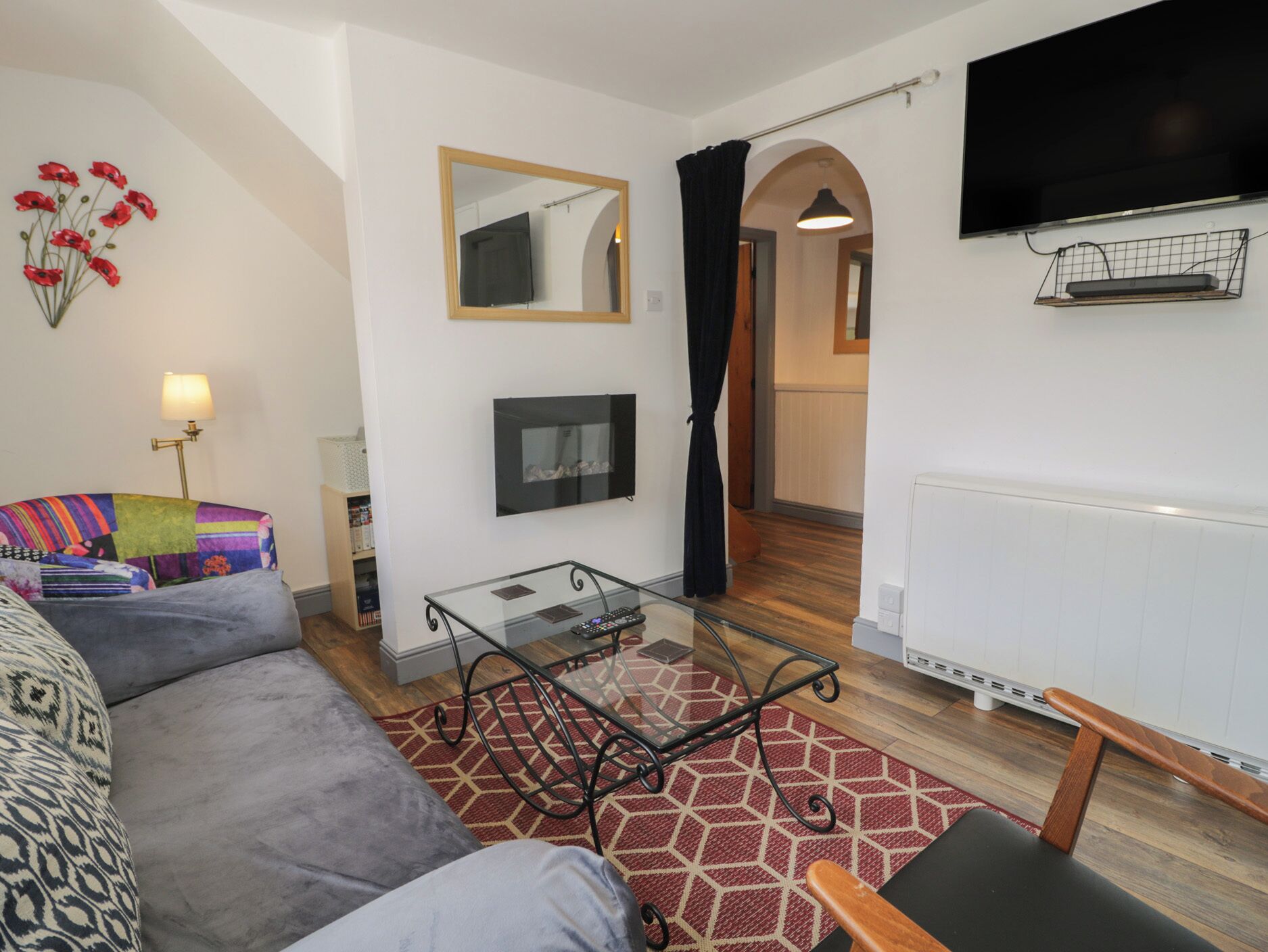 A modern living room with a sofa, a glass coffee table, a flat-screen TV, and a small TV on a shelf.
