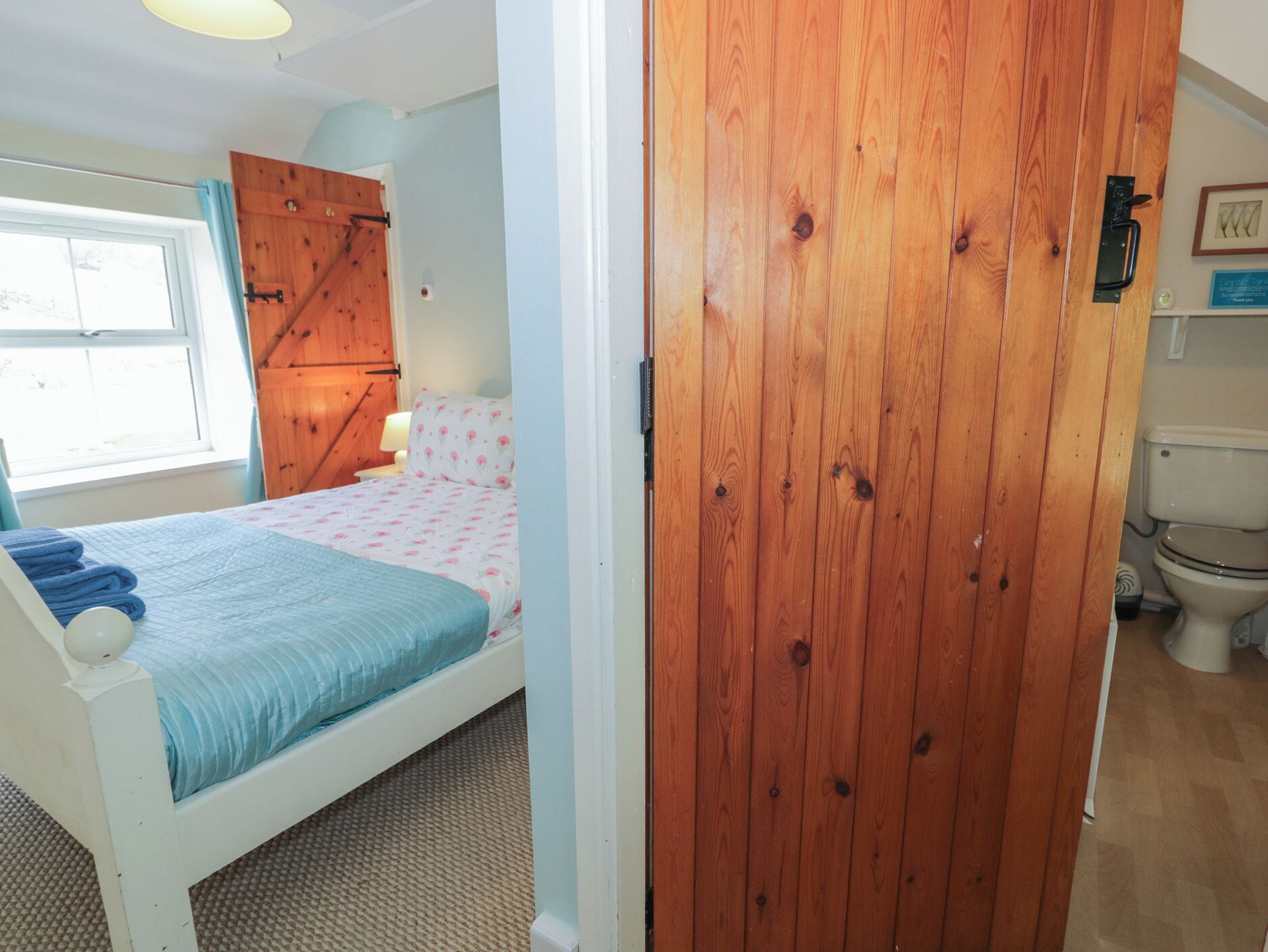 A bedroom with a bed, a wooden door, a window, and a toilet.