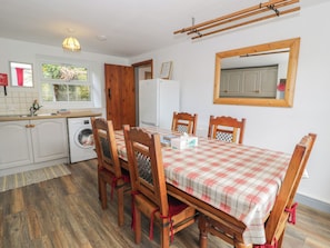 A compact kitchen with a washing machine, a dining table with chairs, and a wooden drying rack. - Ysgoldy (Dolwyddelan)