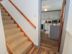 Una escalera conduce a una cocina con piso de madera, gabinetes blancos y una lámpara colgante.