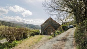 A stone building with a triangular roof, a paved path, and a vehicle parked nearby. - Ysgoldy (Dolwyddelan)